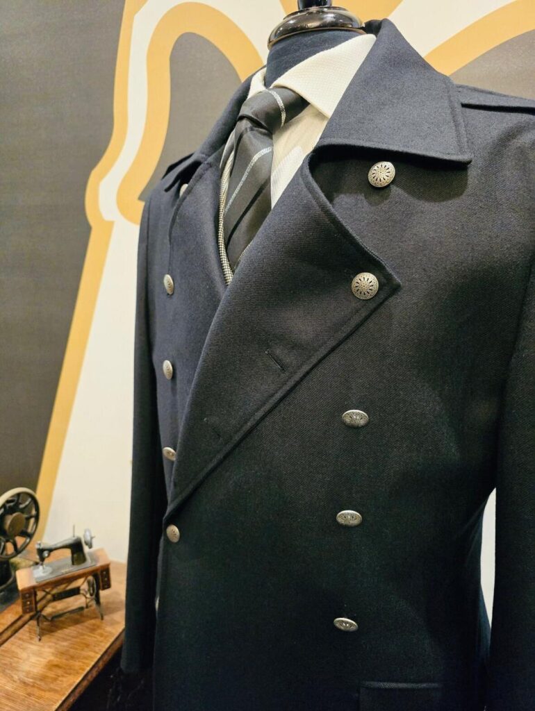 Close-up of a bespoke navy overcoat with silver buttons, paired with a stylish striped tie. The high-quality fabric and precise tailoring create a sophisticated and timeless look, perfect for formal or business occasions.